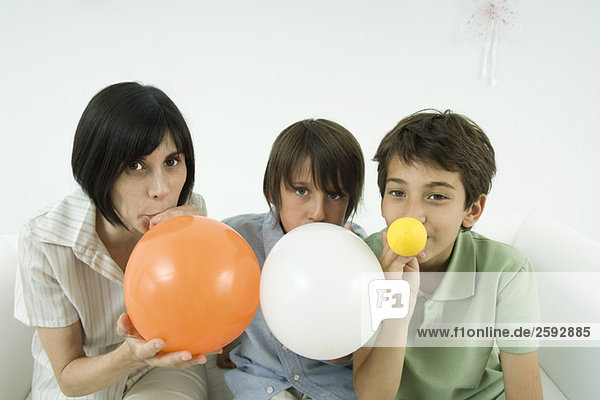 Mutter und zwei Söhne beim Aufblasen von Luftballons  Blick in die Kamera