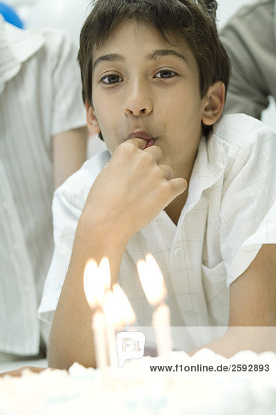Junge vor dem Geburtstagskuchen mit angezündeten Kerzen  Verkostung der Glasur mit dem Finger