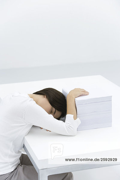Frau schläft am Schreibtisch  Hand ruht auf großem Papierstapel