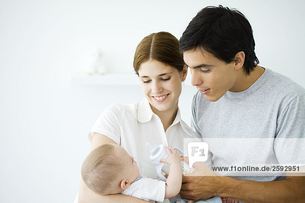Junge Eltern lächeln Baby an  Vater hilft Baby halten Flasche