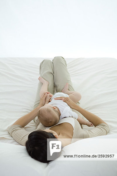 Woman lying on bed  holding infant on her stomach  rear view