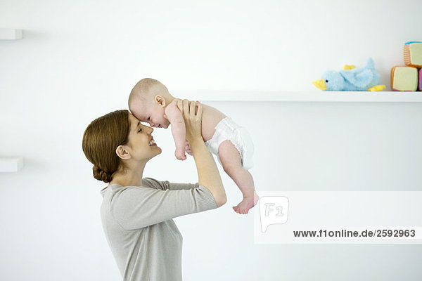 Mother lifting baby in the air  touching foreheads  side view