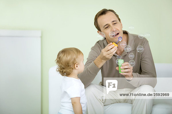 Father and toddler blowing bubbles together