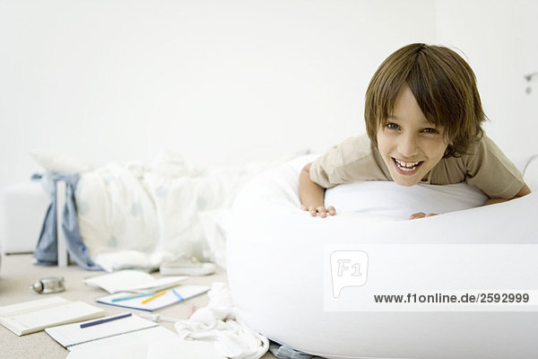 Boy lying on stomach in messy room  smiling at camera