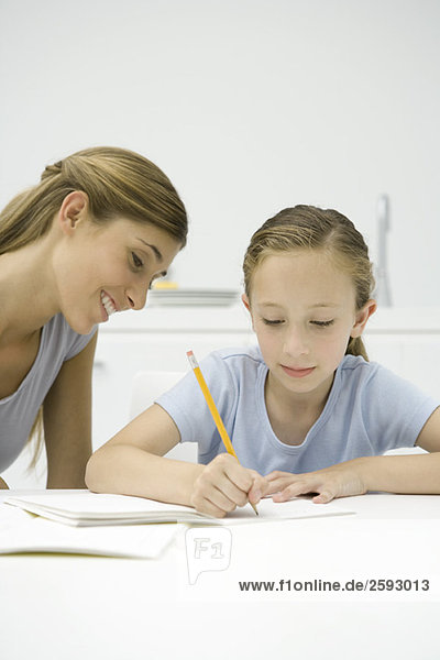 Mädchen macht Hausaufgaben bei Tisch  Mutter schaut zu