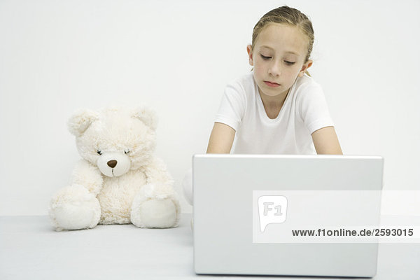 Mädchen sitzend neben Teddybär  mit Laptop-Computer