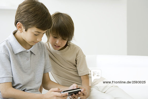Zwei Jungen spielen zusammen Handheld-Videospiel