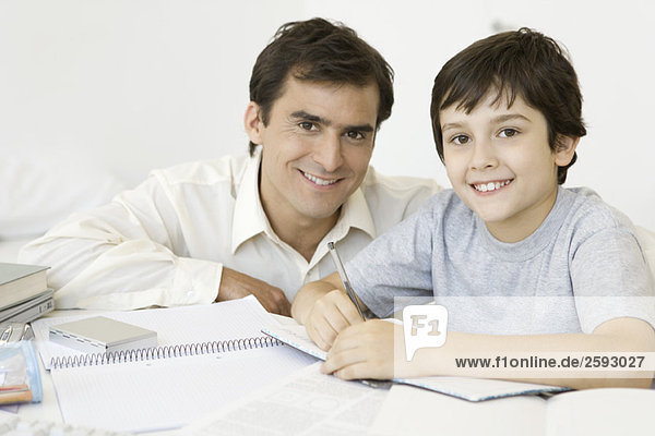 Junge macht Hausaufgaben mit Vater  beide lächeln vor der Kamera