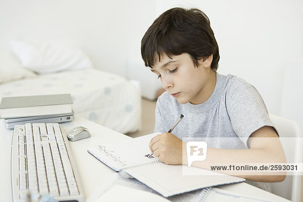 Junge sitzt am Schreibtisch im Schlafzimmer  kritzelt im Notizbuch