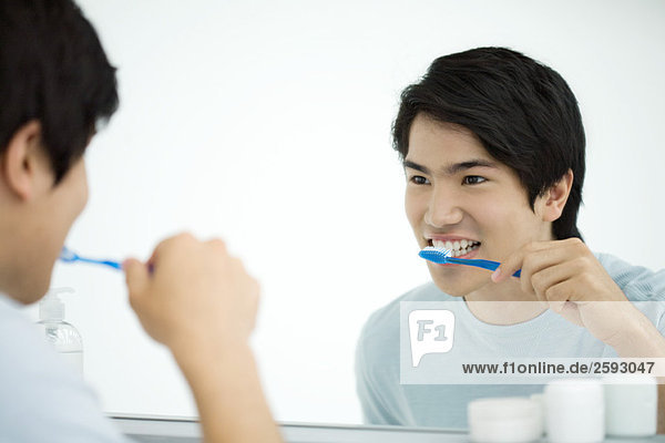 Junger Mann beim Zähneputzen  sich selbst im Spiegel betrachtend