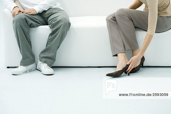 Mann und Frau sitzen auf dem Sofa  Frau zieht Schuhe an  Blick in den Ausschnitt