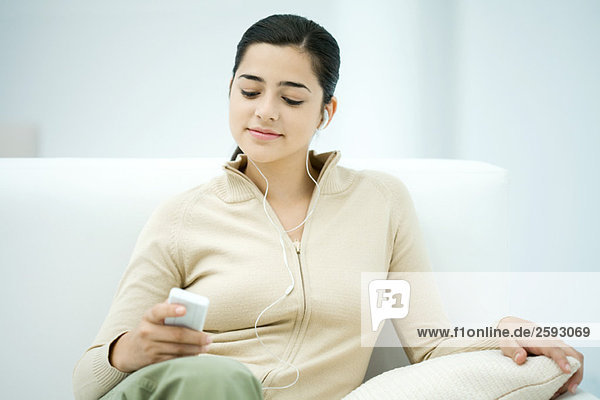 Junge Frau sitzt auf dem Sofa und hört den MP3-Player.