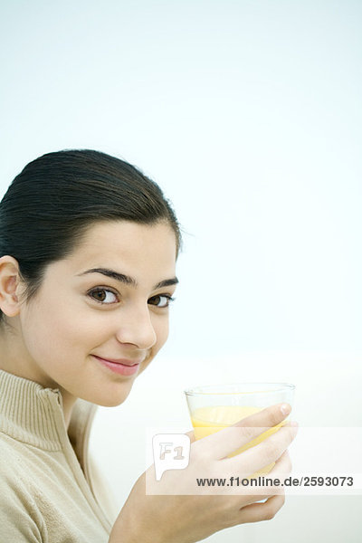 Junge Frau mit einem Glas Orangensaft  lächelnd vor der Kamera