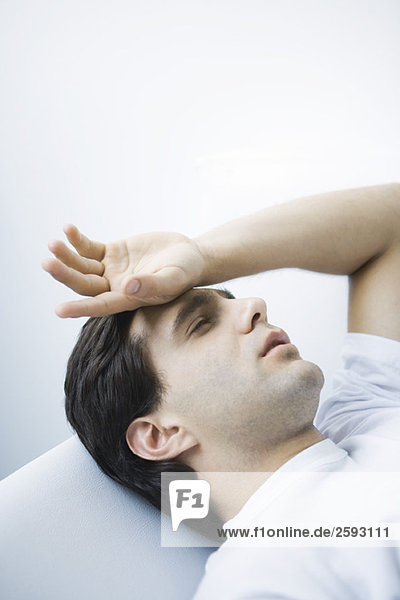 Mann liegend mit geschlossenen Augen  Hand auf Stirn