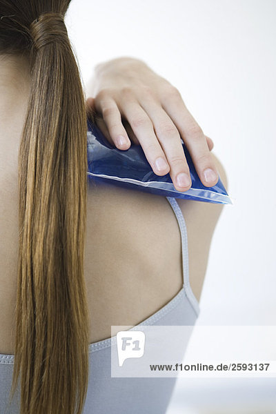 Woman holding cold compress against shoulder  cropped rear view
