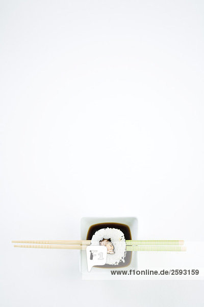 Einzelstück Maki-Sushi auf Essstäbchen über Sojasauce  Draufsicht