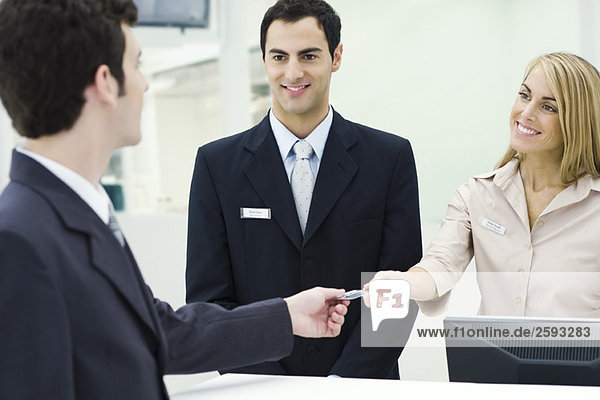Mann  der lächelnden Kundendienstmitarbeitern eine Kreditkarte gibt.