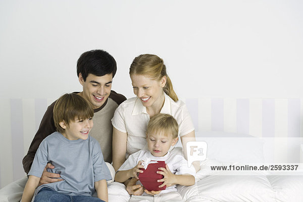 Eltern und zwei Kinder  die zusammen auf dem Bett sitzen  ein Junge mit Geschenk