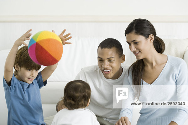Family gathered around toddler girl  smiling  boy throwing ball in the air