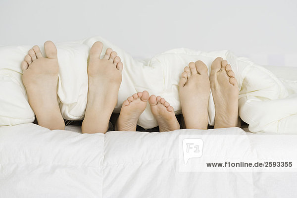 Kind liegt zwischen den Eltern unter der Bettdecke  nur nackte Füße ragen heraus.