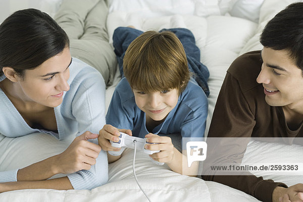 Family lying together on bed  boy playing video game