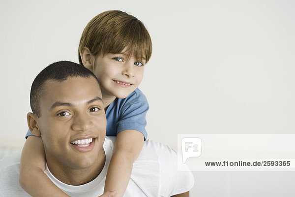 Boy leaning over father's shoulders  both smiling  portrait