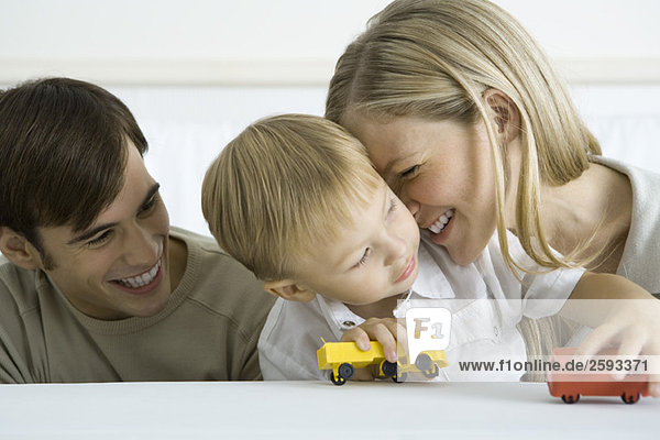 Little boy sitting with parents  playing with toy trucks  mother nuzzling his cheek