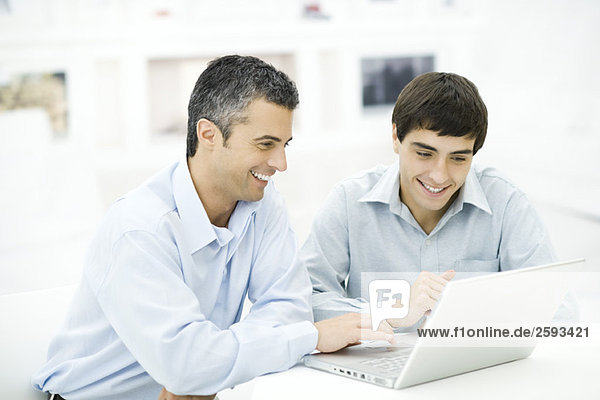 Father and adult son looking at laptop computer together  smiling