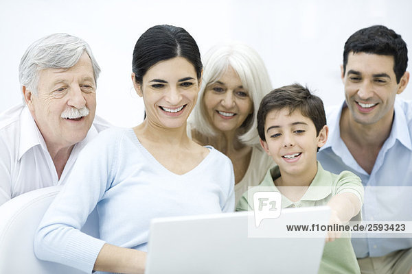 Multi-generation family gathered around laptop computer  smiling