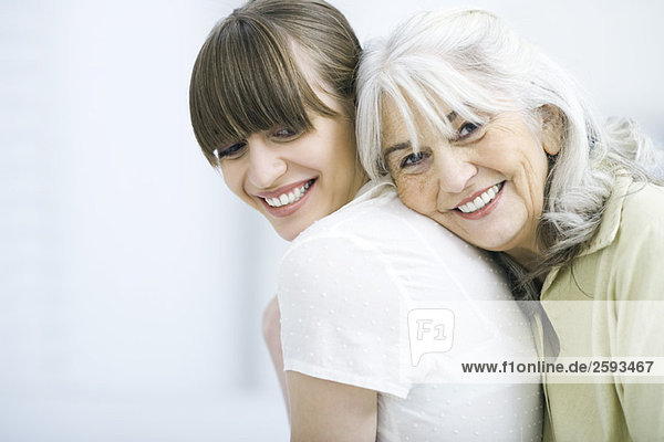 Senior woman leaning against adult daughter's back  smiling at camera