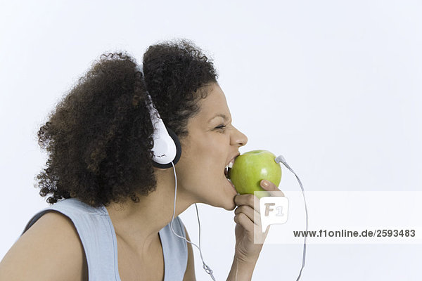 Frau trägt Kopfhörer in Apfel gesteckt  beißt in Apfel  Profil