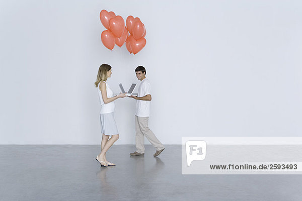 Man and woman walking toward each other with laptop computers and heart balloons  smiling