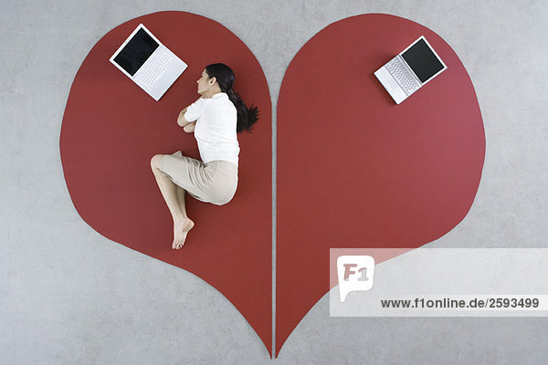 Frau auf dem Boden liegend mit Laptop auf großem gebrochenem Herzen  verlassener Laptop hinter ihr