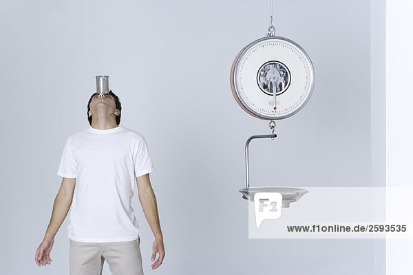 Man standing beside empty scale  balancing can on forehead