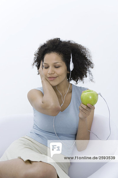 Frau hört Kopfhörer an Apfel angeschlossen  Augen geschlossen