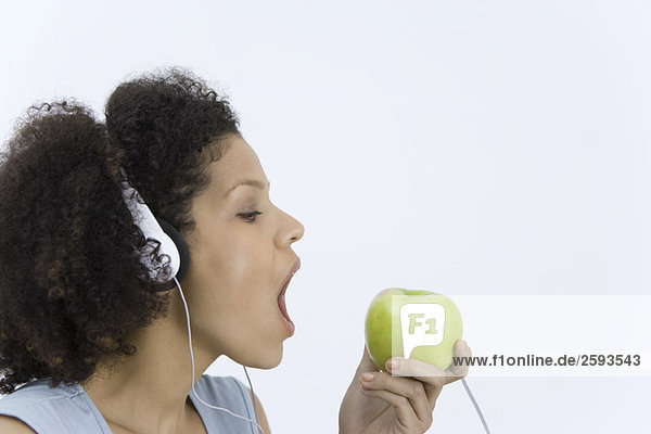 Frau hört Kopfhörer an Apfel  Mund offen  Profil