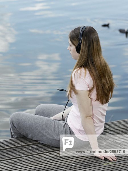 Eine junge Frau  die Kopfhörer trägt und am Steg sitzt.