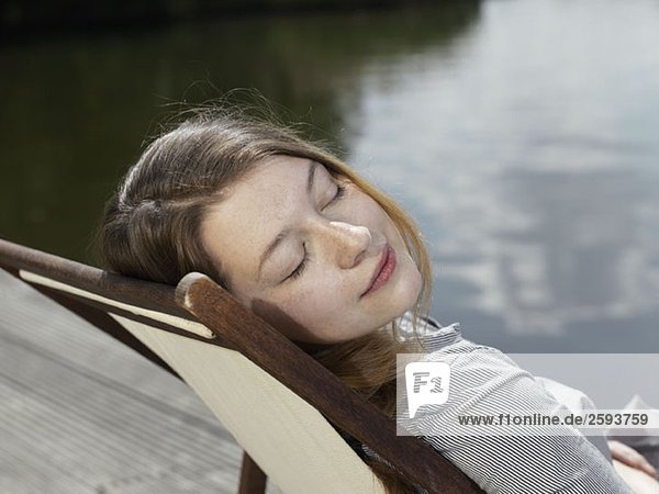 Eine junge Frau sitzt in einem Liegestuhl  die Augen geschlossen.