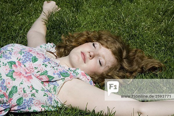 Eine junge Frau  die mit ausgestreckten Armen im Gras liegt.