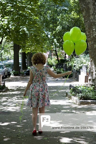 Eine junge Frau auf einem Bürgersteig mit Luftballons  Rückansicht
