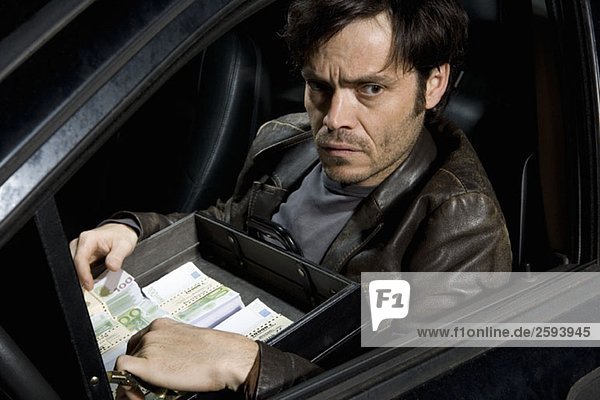 Ein Mann sitzt in einem Auto mit einer offenen Aktentasche voller Geld.