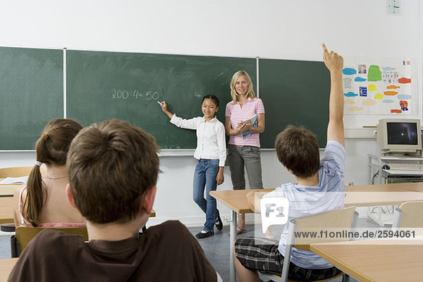 A teacher and a student at the blackboard  facing the class