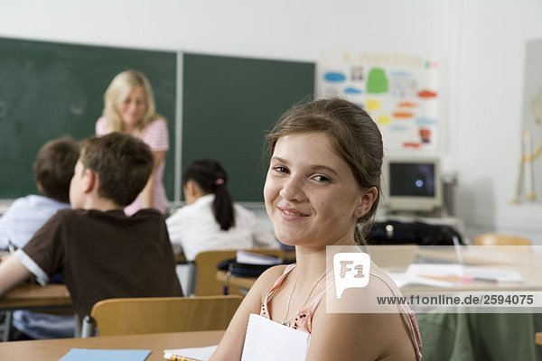 A pre-adolescent girl sitting in the back of a classroom  looking at camera