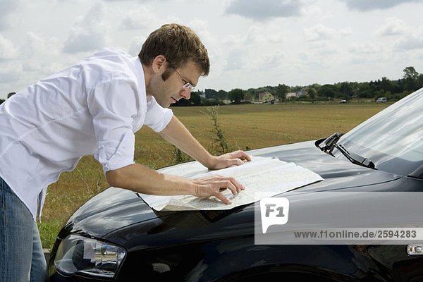 A man leaning on a car bonnet and reading a map