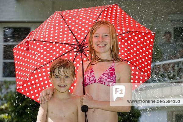 Zwei Kinder stehen unter einem Regenschirm in ihren Badeanzügen.
