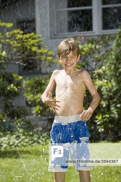 Ein kleiner Junge steht in einer Sprinkleranlage.