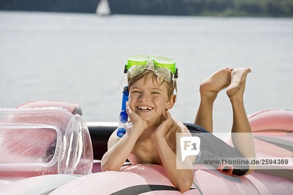 Ein kleiner Junge  der auf einem Schlauchboot auf einem See liegt.