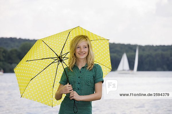 Ein junges Mädchen steht an einem See unter einem Regenschirm  bedeckt