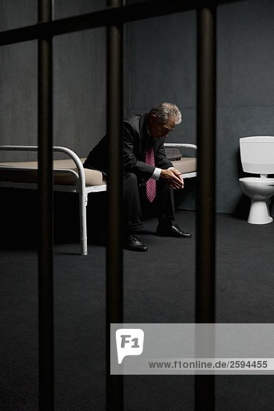 Ein Geschäftsmann sitzt auf einem Bett in einer Gefängniszelle.