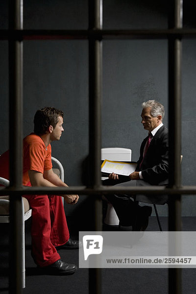 Ein Gefangener  der mit einem Anwalt in einer Gefängniszelle spricht.